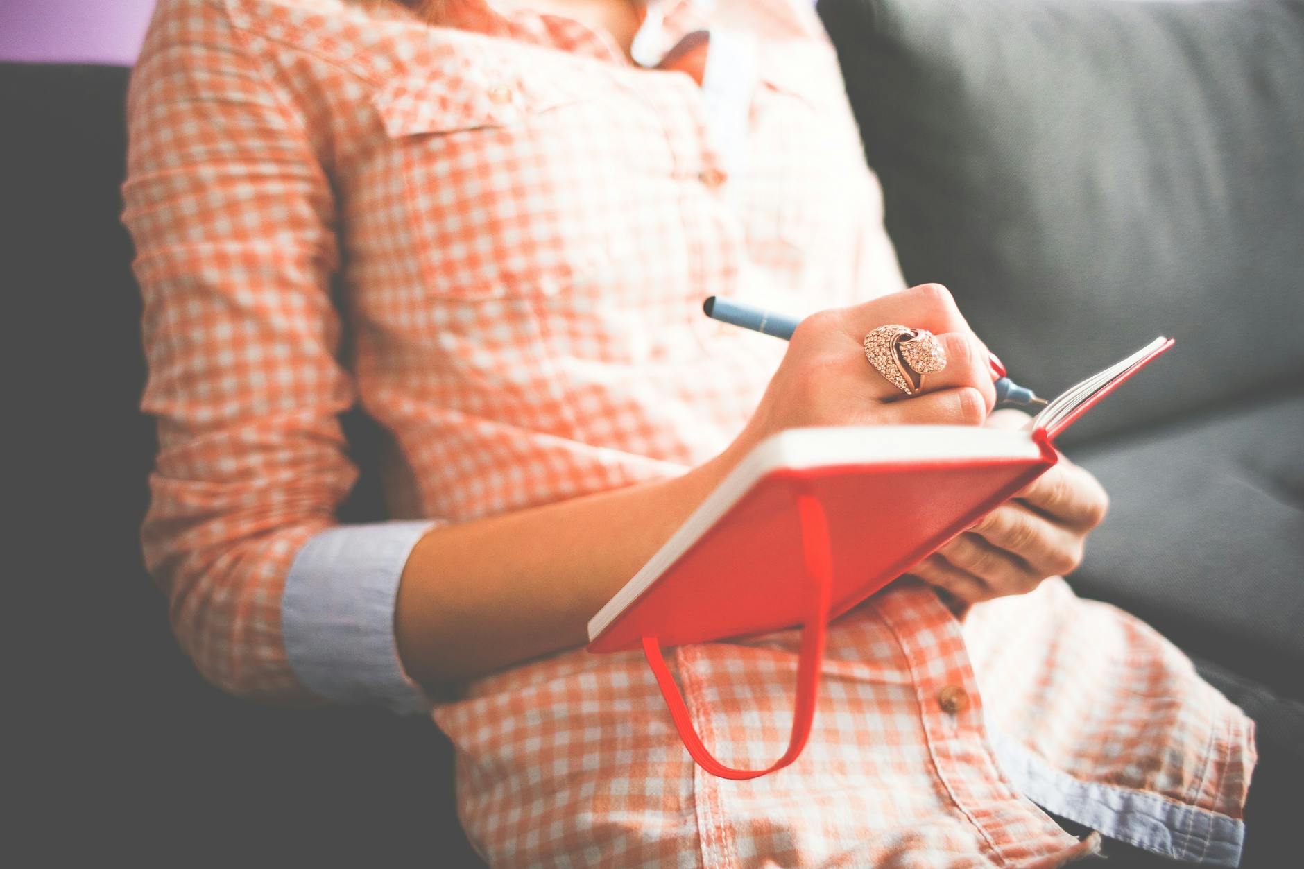 person writing on red notebook